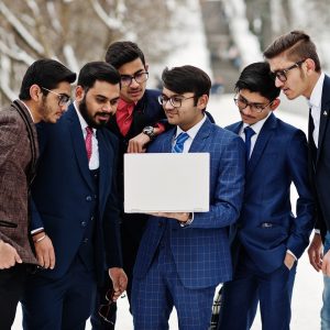 Group of six indian businessman in suits posed outdoor in winter day at Europe, looking on laptop.